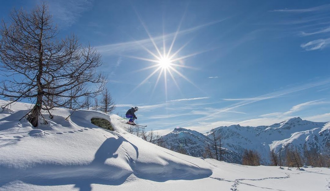 A vibrant winter sports scene at Rothwald, Wasenalp in Switzerland, with a skier gracefully descending on a sunny day. A chalet can be seen nestled in the snowy landscape.