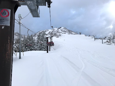 A wintery scene in Suhara Japan showing a buzzing ski resort. A ski lift can be seen against the backdrop of picturesque mountains and snow-coated slopes embodying the thrill of winter sports.