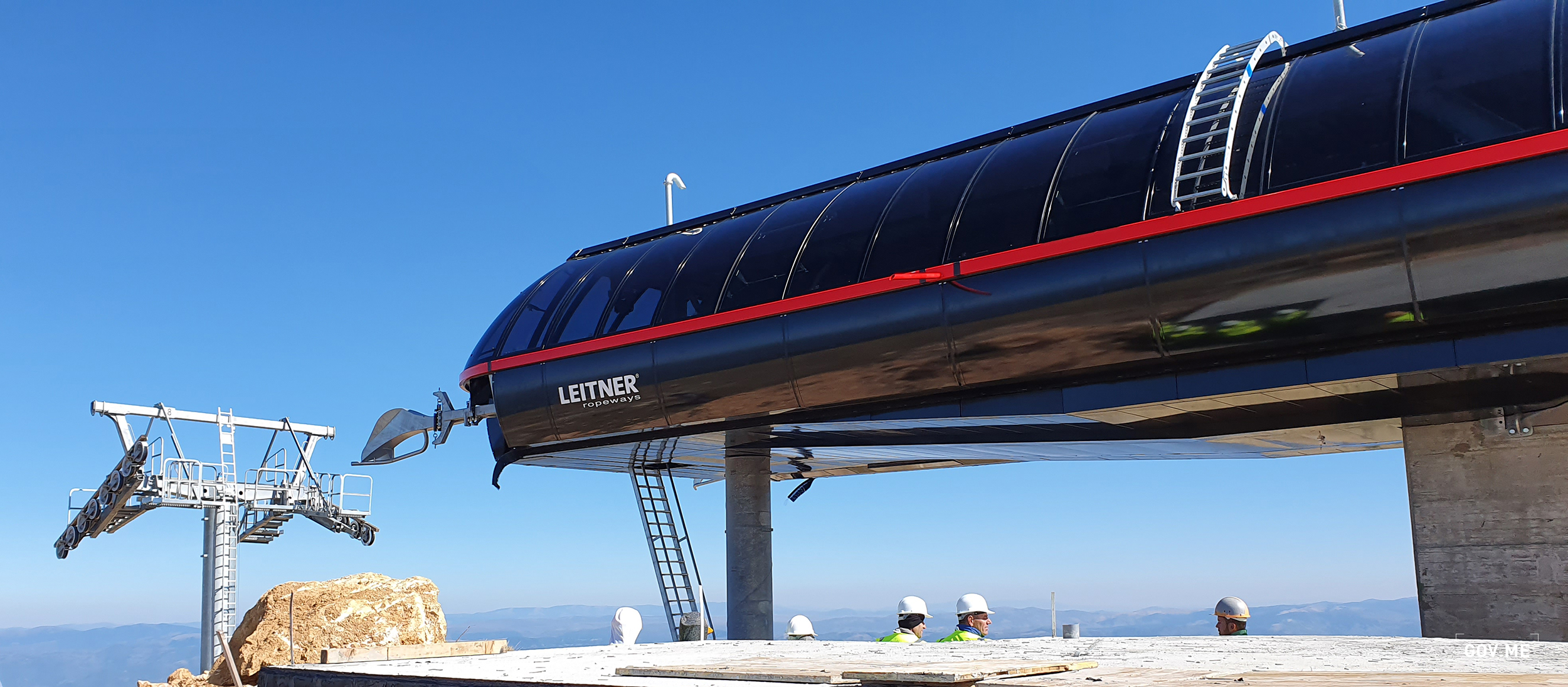 Ski lift ascending the snowy mountain slopes at Cmiljača Ski Center in Rakita, Montenegro. A snowmobile is visible nearby a traditional chalet, while a lone skier navigates the glistening snow.
