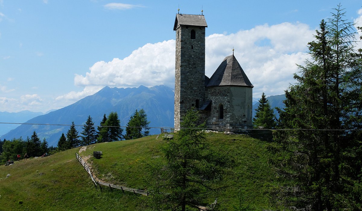 Vigiljoch – Lana in Italy - a church on a hill with mountains in the background.