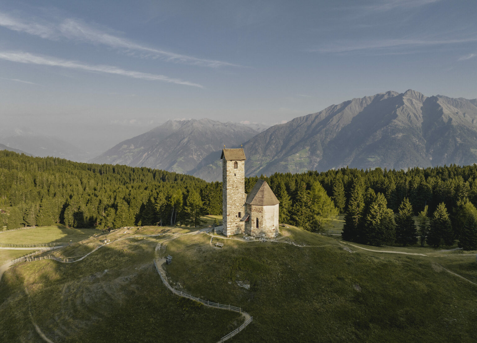 A serene scene at Vigiljoch-Lana in South Tyrol Italy showcasing a charming chalet nestled against the backdrop of a majestic mountain. It's a beautiful sunny day with clear blue skies.