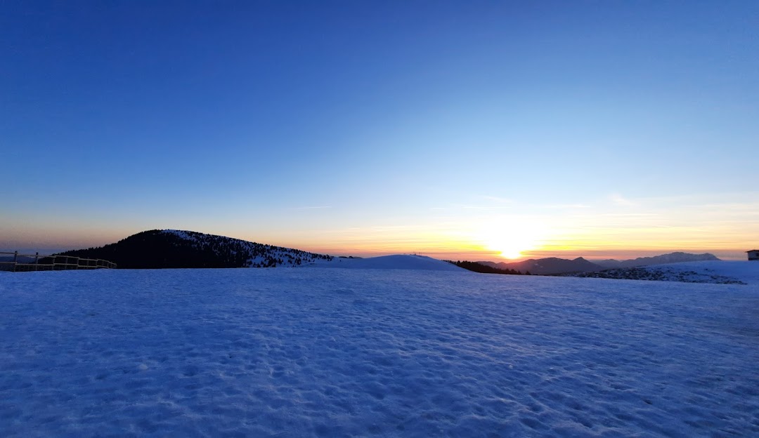 Winter landscape at Monte Pora in Lombardy, Italy, featuring a charming chalet nestled amongst snow-covered trees with a mountainous backdrop, typifying a serene scene of winter sports and alpine beauty.
