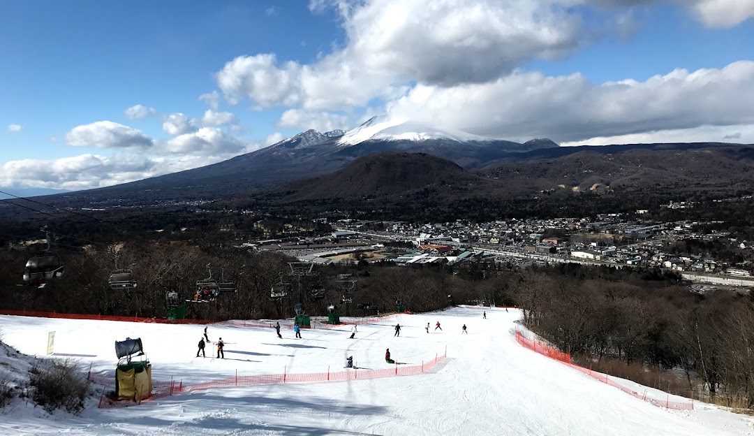 View of a bustling winter sports scene at a ski resort in Karuizawa, Japan, featuring a chalet nestled at the foot of a mountain.