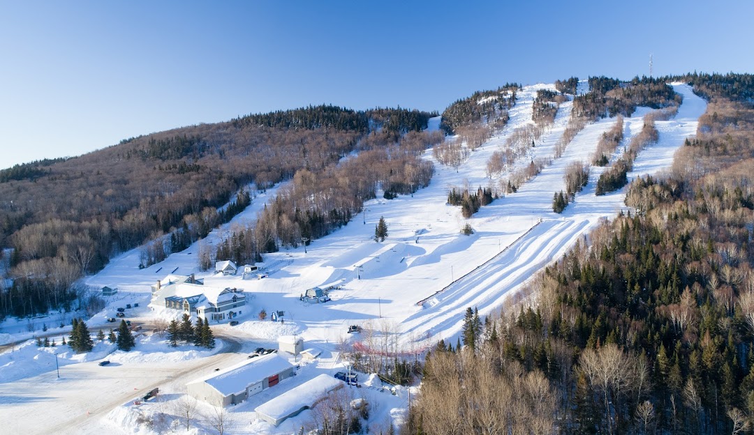 Ski La Réserve Resort in Quebec, blanketed by a thick layer of snow. Winter sports enthusiasts are visible on the snow-covered slopes and a ski lift quietly shuffles people back to the top.