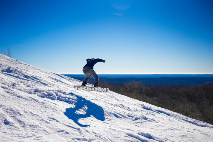 A snowboarder taking on the snowy slopes at Caberfae Peaks in Cadillac, Michigan. He is perfectly balanced mid-action, carving a path through the pristine white snow.