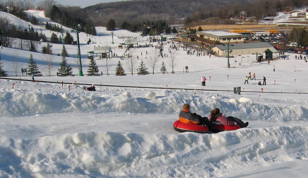 Winter sports enthusiasts enjoying the day at Mt Kato Ski Resort in Mankato, Minnesota, featuring snow-covered slopes and a cozy chalet, set against a snowy landscape.