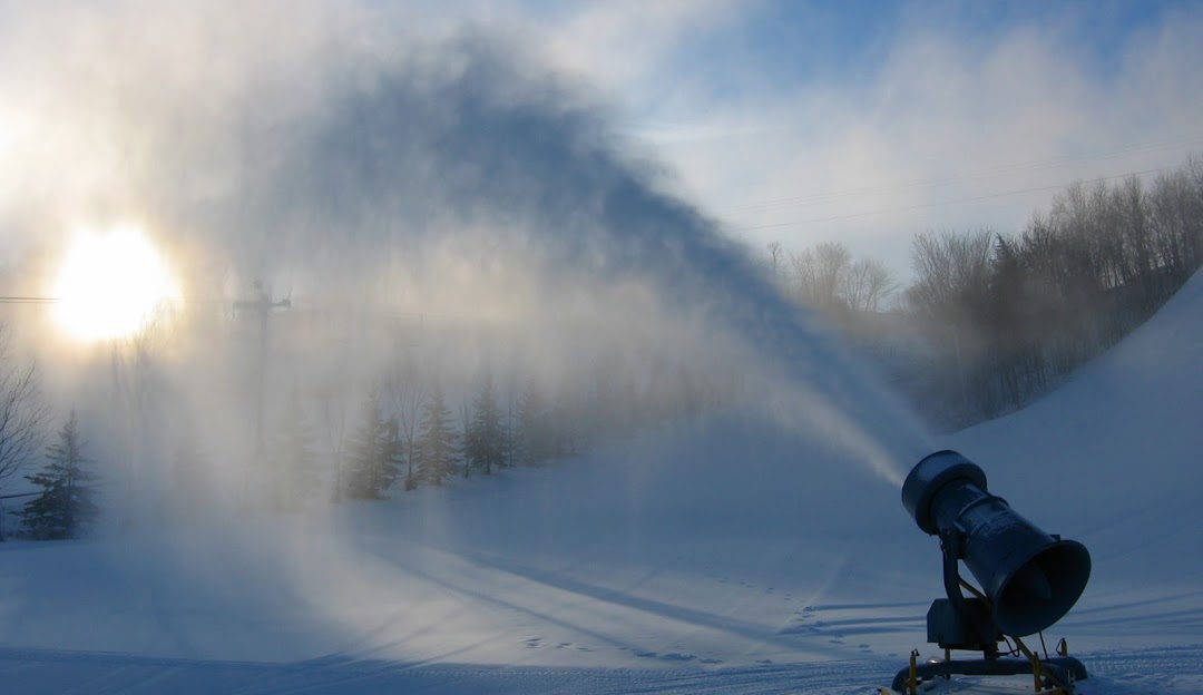 Winter scene at Mt Kato ski resort in Mankato, Minnesota, featuring skiers on snowy slopes and ski lifts, and a snowmobile in the foreground.