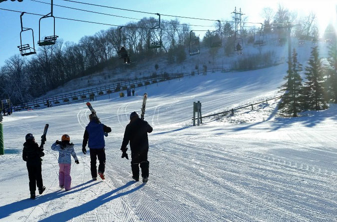 Families enjoying a day of winter sports at Mt Kato ski resort in Mankato Minnesota with a ski lift in the background.