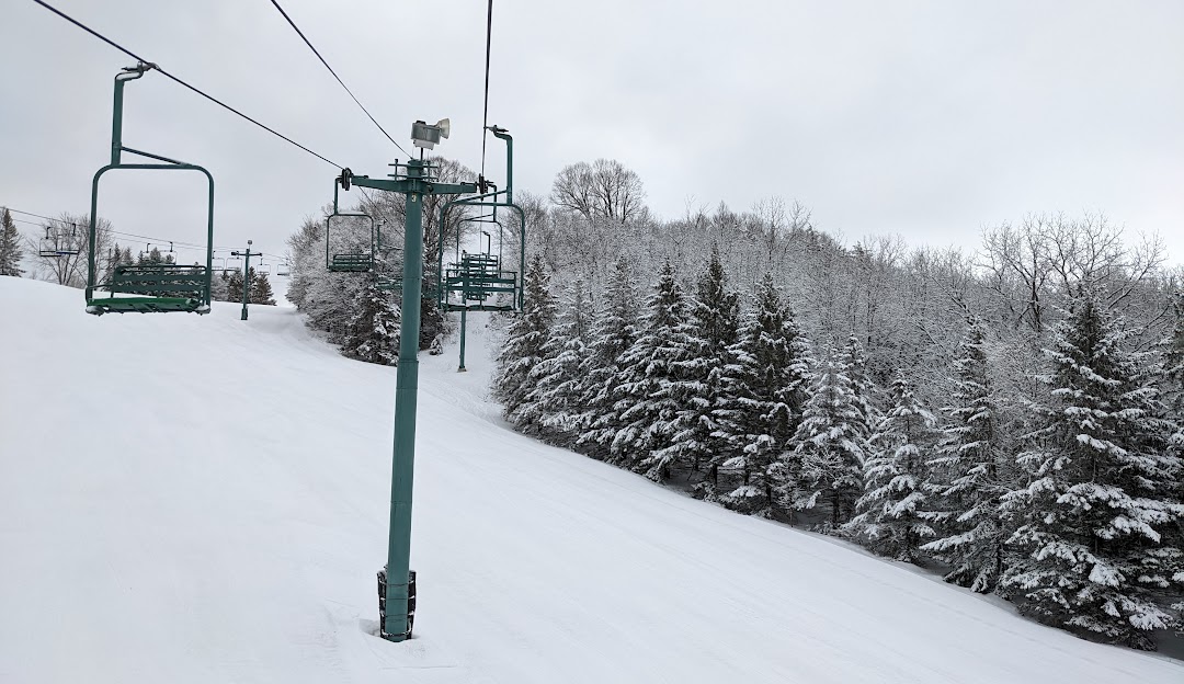 A picturesque view of Mt Kato ski resort in Mankato Minnesota featuring a ski lift ascending the snowy mountain amid a serene winter landscape with a chalet nestled nearby.