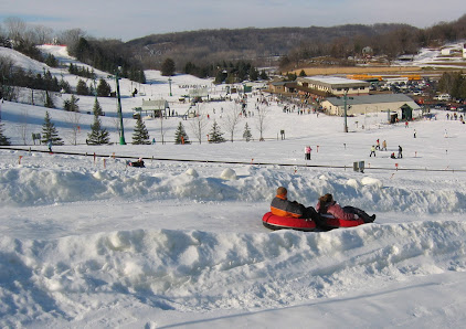 Skiers and snowboarders enjoying a winter's day on the groomed slopes of Mt. Kato in Mankato Minnesota with a snowmobile and the resort's chalet viewable in the background.