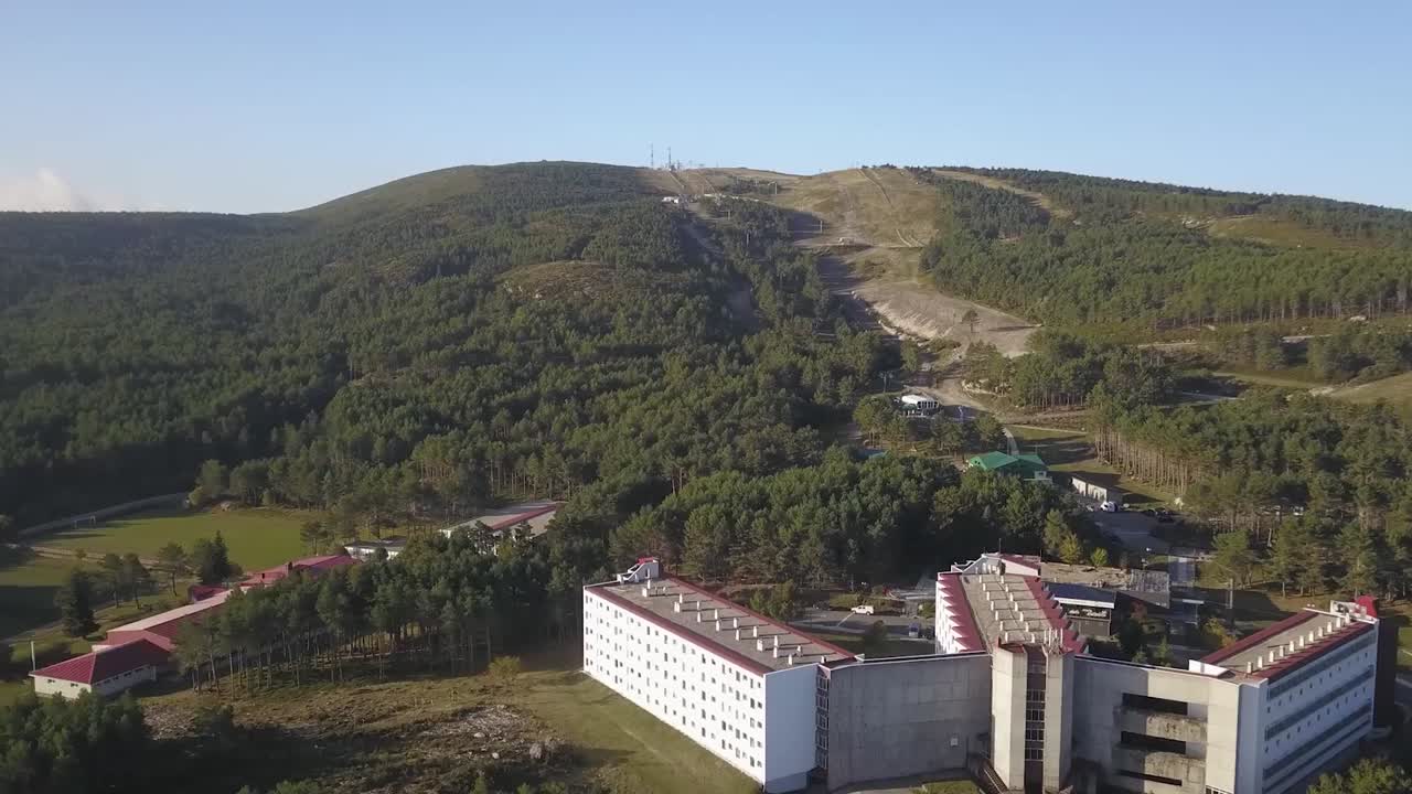 View of the popular Manzaneda ski resort in Ourense, Spain, showcasing a chalet nestled amongst the mountains with a ski lift in the distance.