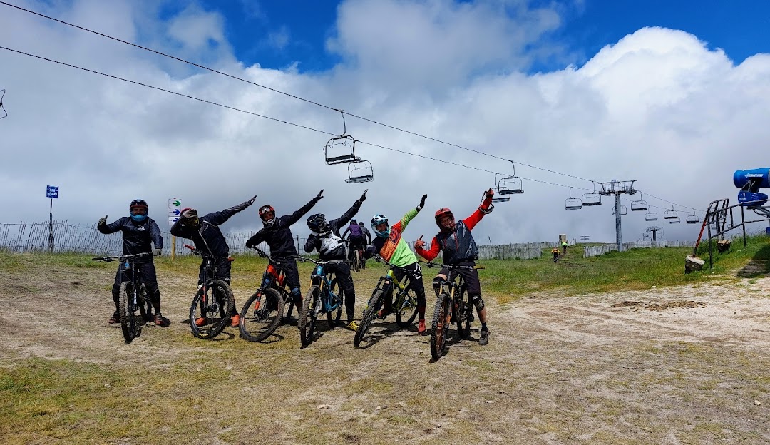 A mountain biker riding near a chalet in Manzaneda, Ourense, Spain. A ski lift is faintly visible in the background, indicating the location's versatility as a winter sports destination.