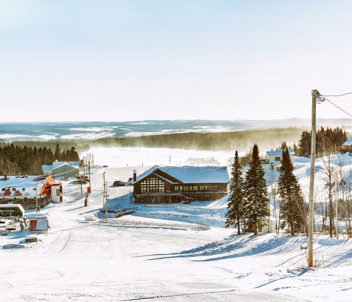 Winter scene at Val d'Irène in Quebec, Canada, showcasing a ski resort bustling with activity. Snow-covered slopes and a ski lift enrich the beautiful winter panorama.