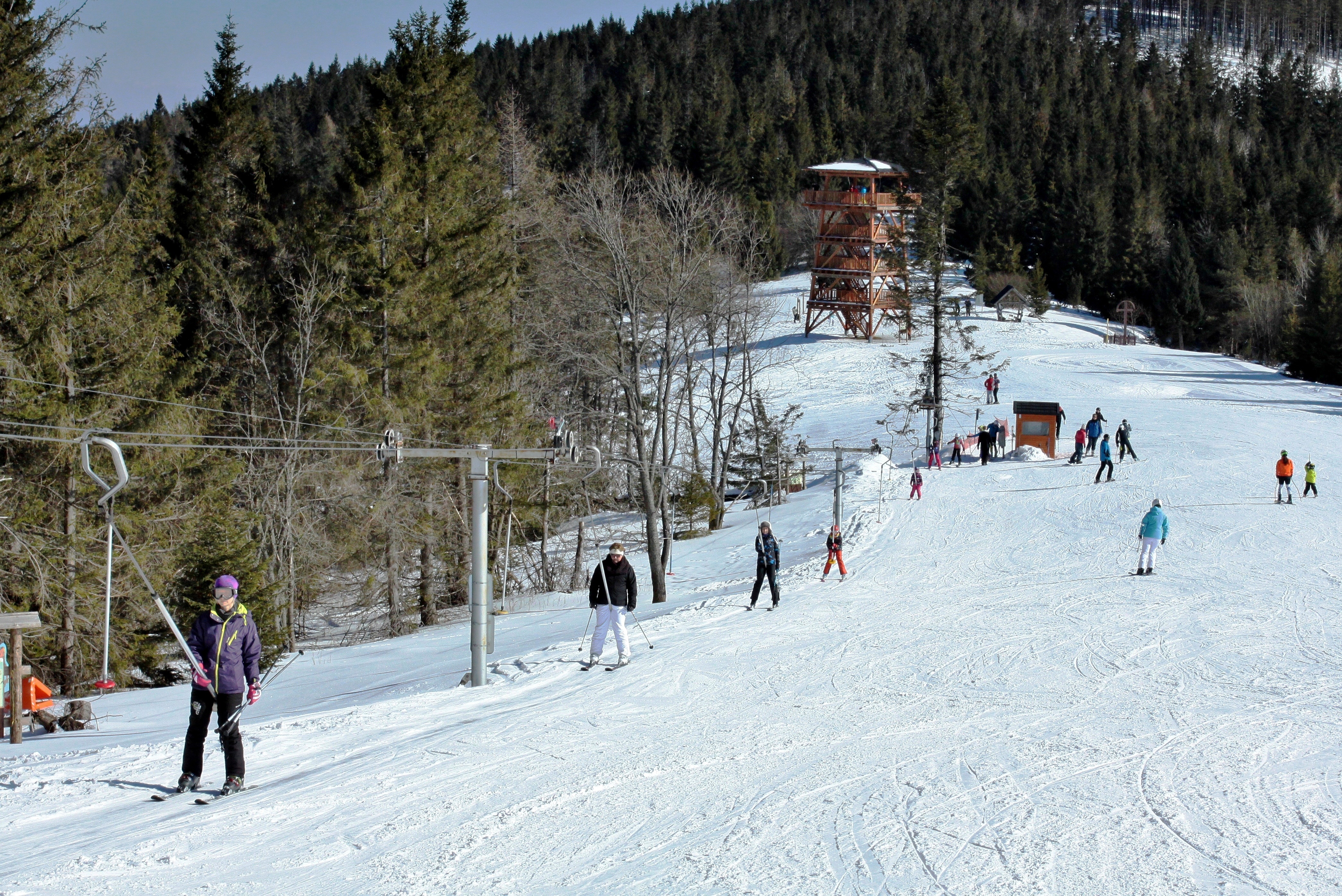 Winter scene at Ski Jezersko - Bachledova dolina resort in Slovakia, featuring skiers on the slopes, a ski lift, a challet, and a winter sports centre.