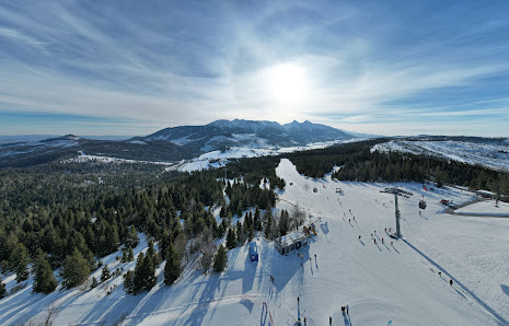 An inviting view at the Ski Jezersko - Bachledova dolina resort in Slovakia, featuring a bustling winter sports scene, a ski lift, and a cozy chalet amidst snow-covered slopes.