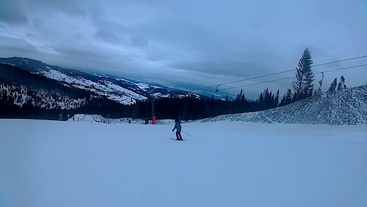 A skier enjoying the winter sports scene at Ski Jezersko - Bachledova dolina in Slovakia, with a ski lift and resort visible amidst stunning winter scenery.