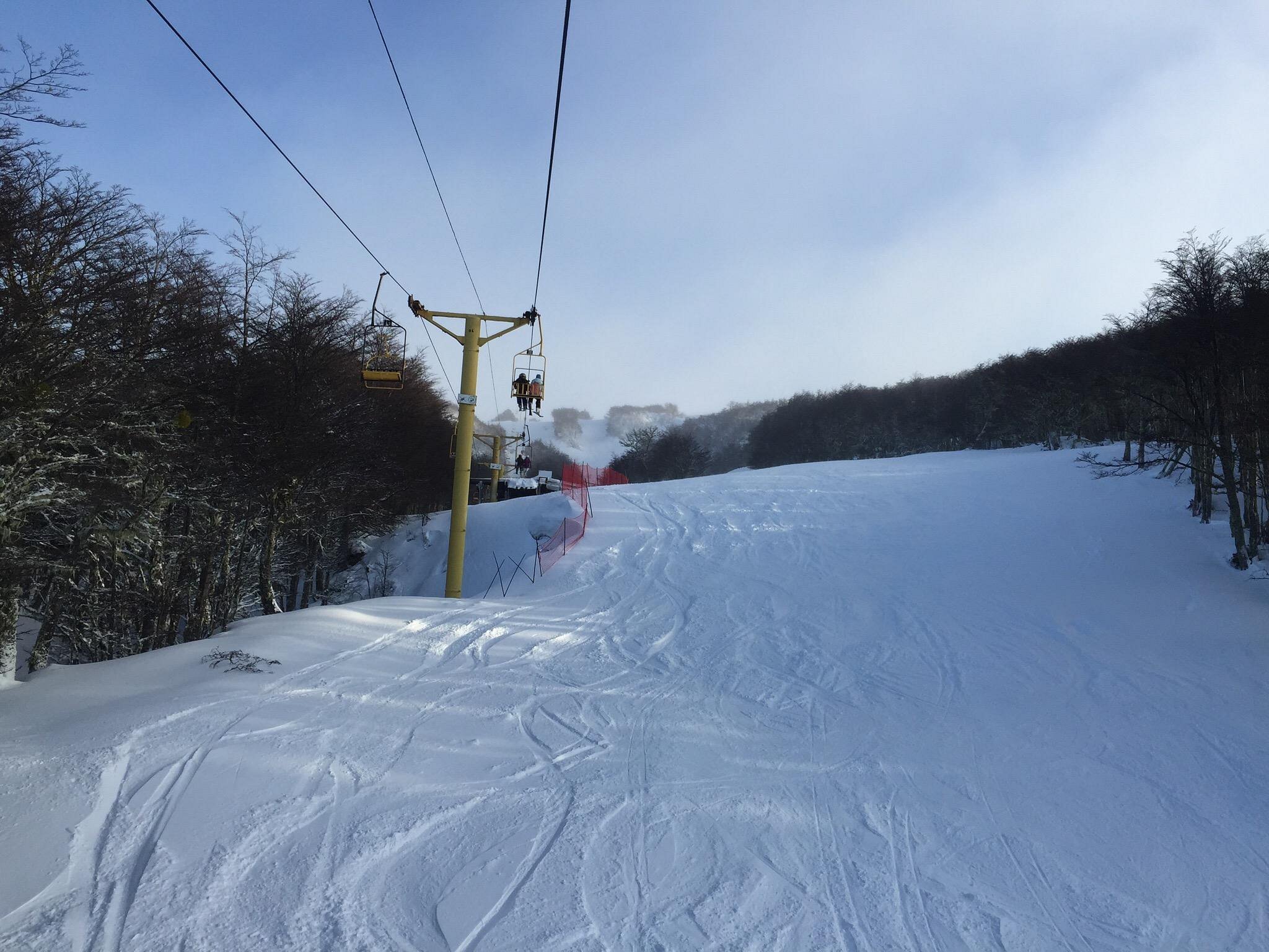 A chalet stands out in the vibrant winter landscape at Club Andino Punta Arenas Chile. Skiers enjoy the slopes while others ascend the mountain on a ski lift.