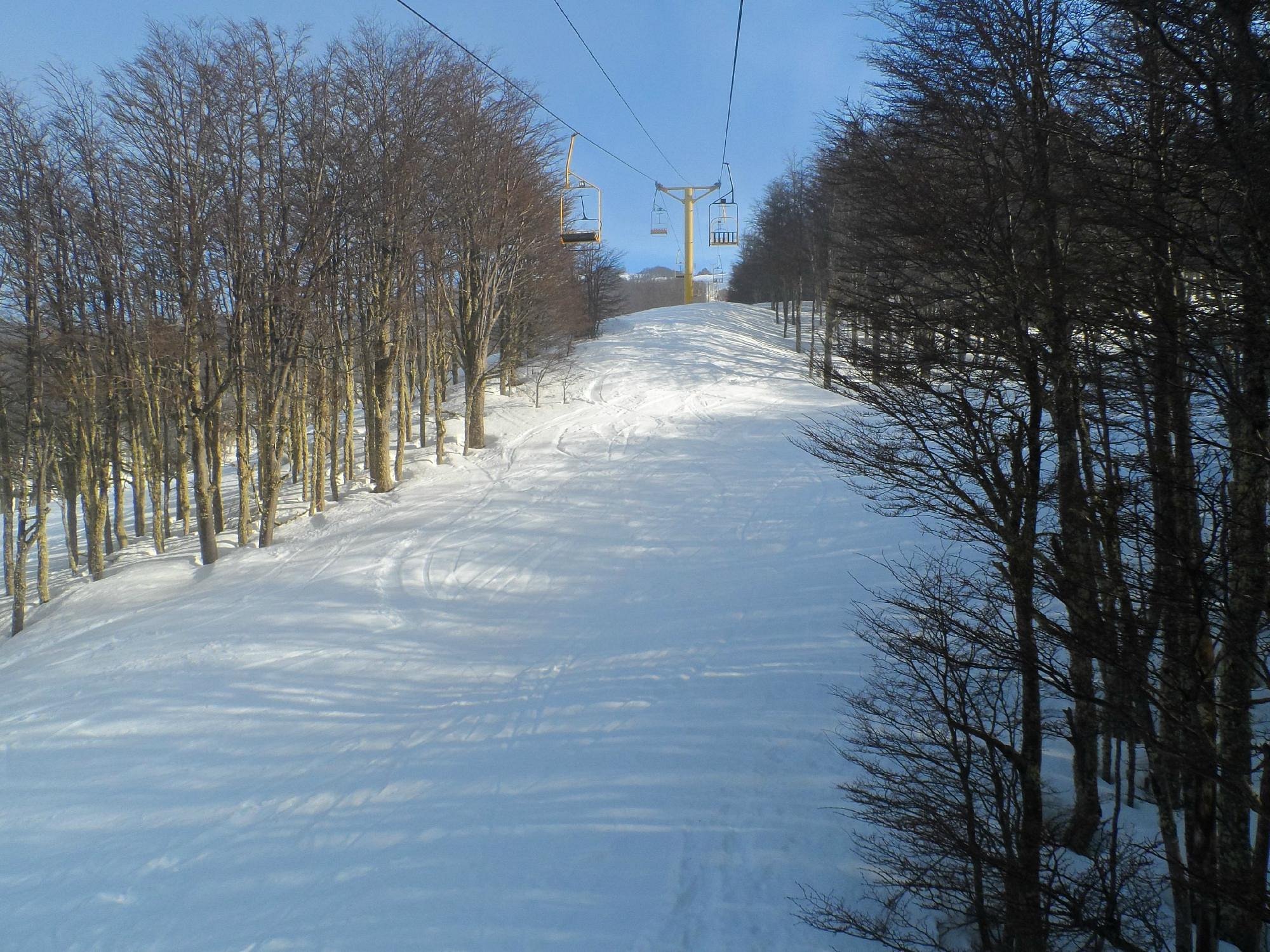 A Chilean winter sports scene at Club Andino ski resort in Cerro Mirador featuring a ski lift a quaint chalet and a skier maneuvering down the snow-covered slope.