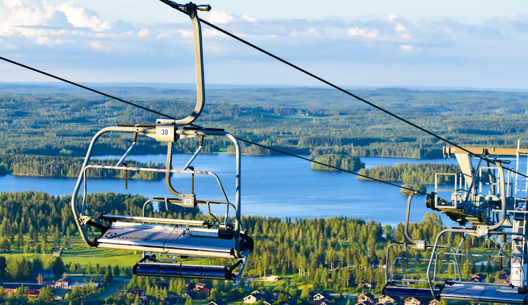 A picturesque scene from Tahko ski resort in Kuopio Finland featuring a ski lift ascending a snow-covered slope. A skier is visible in the distance and a chalet nestles amidst the winter sports scenery.