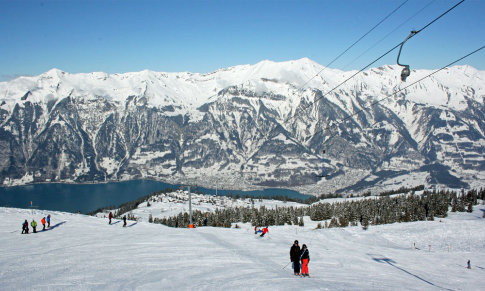 Ski enthusiasts enjoying winter sports at Axalp Tschingellift ski resort in Bernese Oberland, Switzerland, with a ski lift and a charming chalet in view.