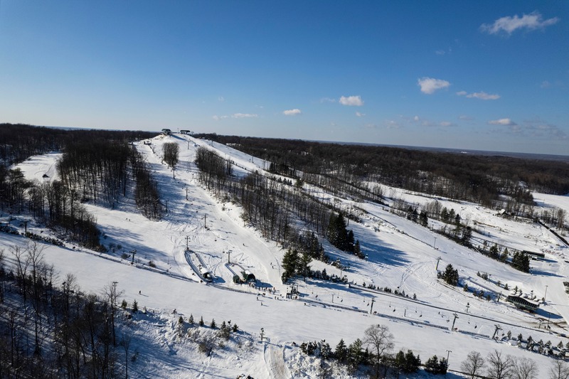 Winter sports scene at Bittersweet Ski Resort in Otsego, Michigan, featuring a skier descending snow-covered slopes with a ski lift in the background.