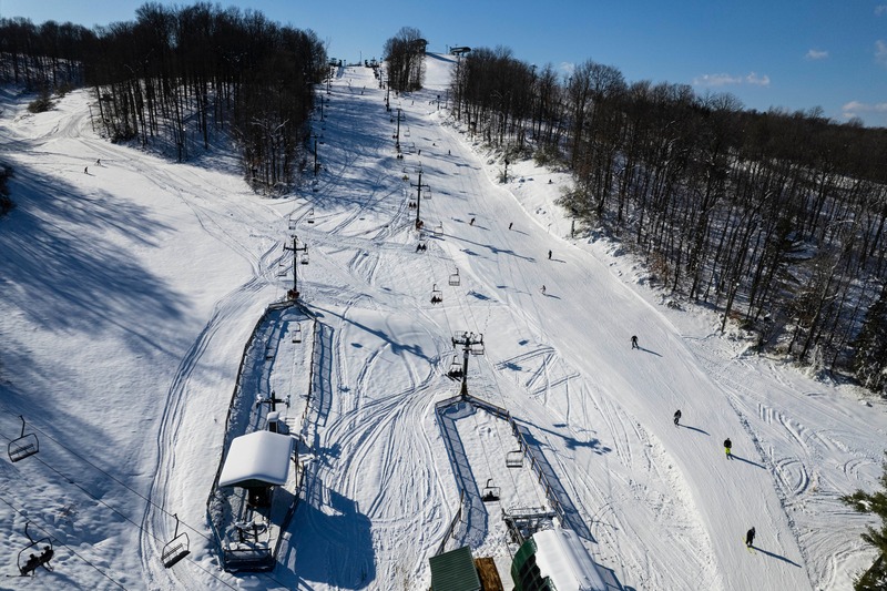A vibrant winter sports scene at Bittersweet ski resort in Otsego Michigan featuring a ski lift traversing over snow-covered slopes with a skier navigating the terrain.