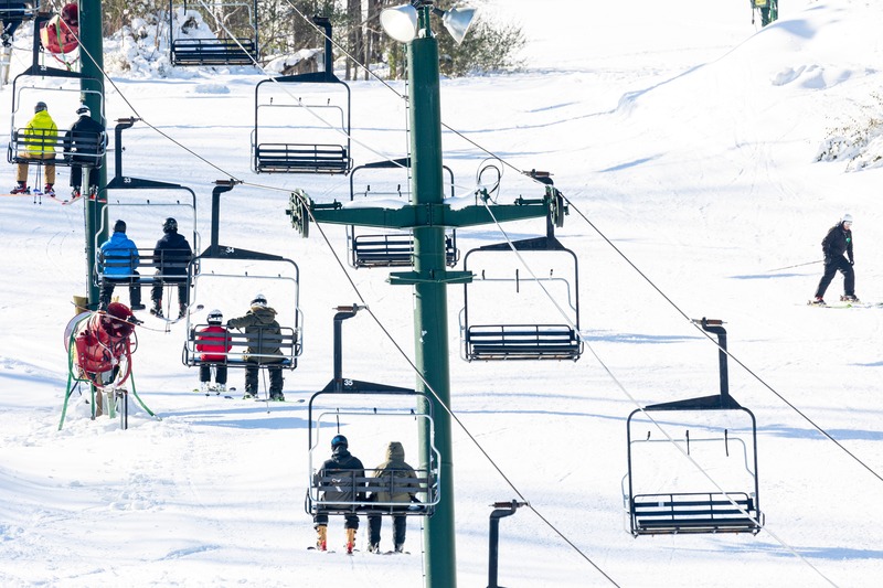 View of Bittersweet ski resort in Otsego Michigan featuring a busy winter sports scene. Visible is a ski lift carrying skiers uphill and skiers descending the snow-covered slopes.