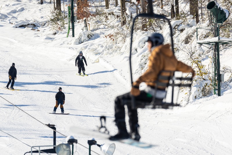 Winter scene at Bittersweet Ski Resort in Otsego, Michigan, with a ski lift in the background and a skier gliding down the slope, enjoying a lively family skiing day.