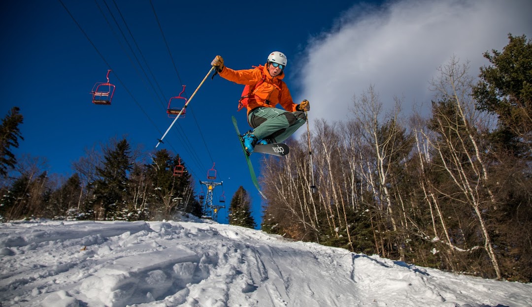 A skier is enjoying a winter sports scene at Black Mountain in Jackson New Hampshire gliding down the snowy slope with the ski lift lightly visible in the background.