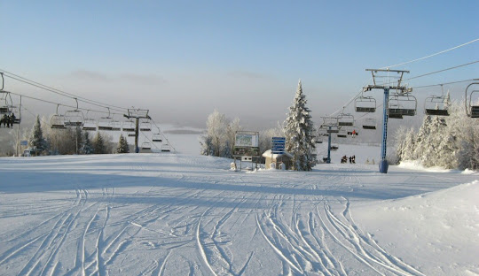 Winter scene at Ski Garceau in Quebec, Canada, showcasing the ski resort filled with enthusiasts, a busy ski lift, and a charming challet nearby, illustrating a lively winter sports centre.