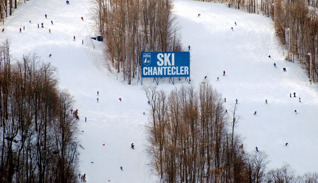 A skier glides down the slopes at Ski Chantecler in Quebec, Canada, surrounded by a captivating winter landscape. The ski resort and lift are visible in the background.
