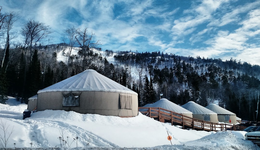View of Mt Bohemia in Mohawk, Michigan featuring a bustling winter sports center and ski resort, surrounded by stunning snow-capped scenery. A cozy mountain hut can be spotted amidst the wintery landscape.