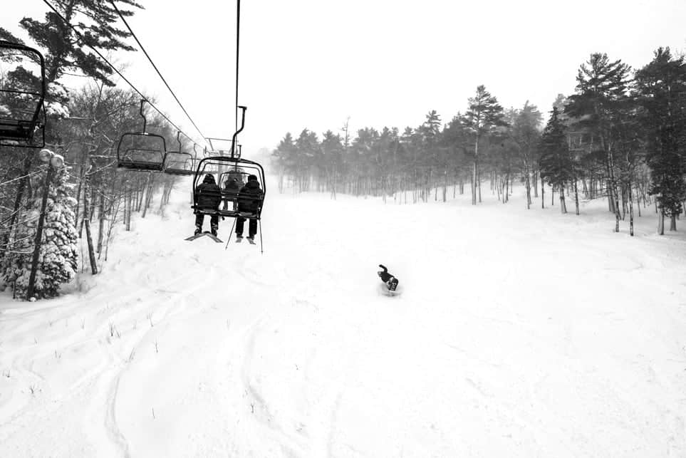 A vibrant winter sports scene captured at Mt Bohemia in Michigan showcasing a ski lift with a skier riding up all set against the backdrop of a ski resort and chalet.