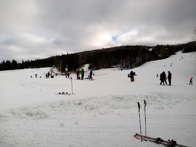A vibrant winter sports scene at Ben Eoin Ski Resort in Nova Scotia, Canada, showcasing a skier navigating the snowy slopes and the cozy chalet nestled in the white landscape.