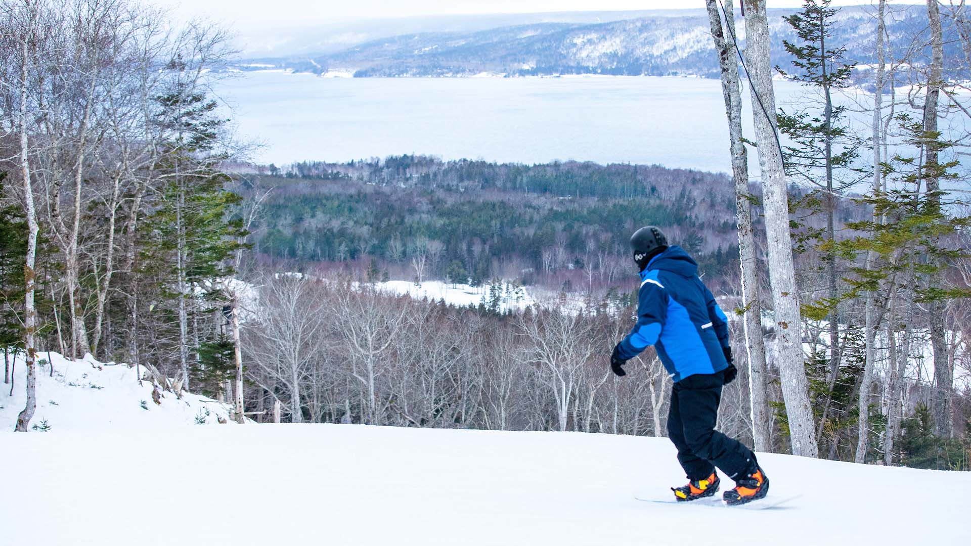 A snowboarder carving through fresh snow on a clear day in Ben Eoin, Nova Scotia, Canada.