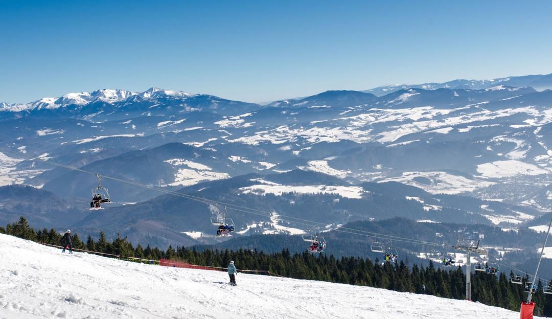 Winter sports scene at Slovakia's Kubínska hoľa ski resort featuring a cozy challet, a skier gliding down the slope and a ski lift in operation.