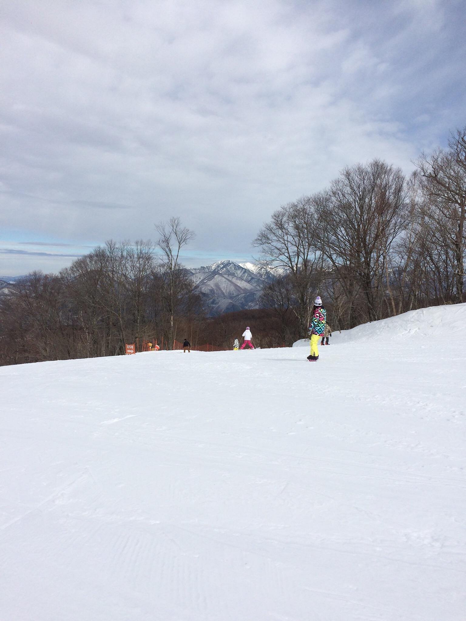A skier and a child learning to ski at Edelweiss in Nikko, Japan. The stunning winter sports scene framed by beautiful mountains includes a charming chalet in the backdrop.