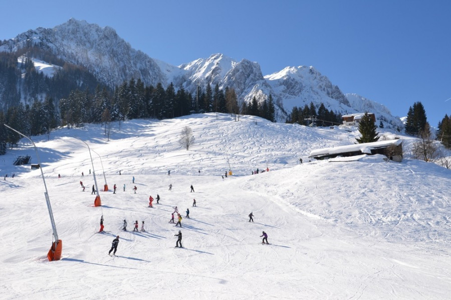 A bustling winter sports scene at Zahmer Kaiser ski resort in Tyrol, Austria, featuring a well-equipped sports center, a cozy chalet in the background, and an active skier maneuvering the snow-covered landscape.