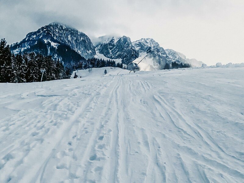 Winter sports enthusiasts in action at Zahmer Kaiser in Austrian Tyrol, surrounded by breathtaking winter scenery. A chalet and various elements of a ski resort subtly complete the picturesque view.