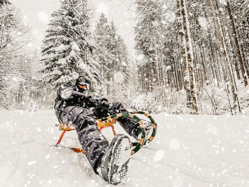 A snowmobile is prominently visible in a winter sports scene at Zahmer Kaiser in Austria. Sparse skiers and a snowboarder can be glimpsed adding to the charming winter atmosphere.