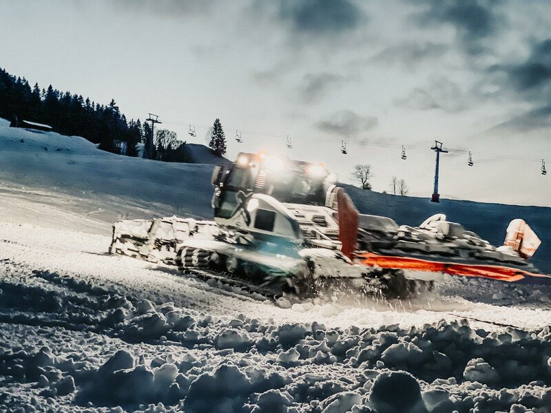 A snowmobile is the central focus in this winter sports scene from Zahmer Kaiser in Tyrol Austria. There's a ski resort in the background with a ski lift and a solitary skier far off in the distance.