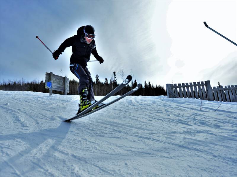 A skier enjoying a winter sports scene at Pin Rouge in Quebec, Canada, with a glimpse of a winter sports centre and chalet nearby.