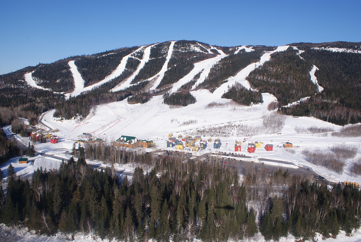 View of Pin Rouge ski resort in New Richmond, Quebec, Canada, featuring a ski lift, filled with winter sports enthusiasts, ascending snow-covered slopes.