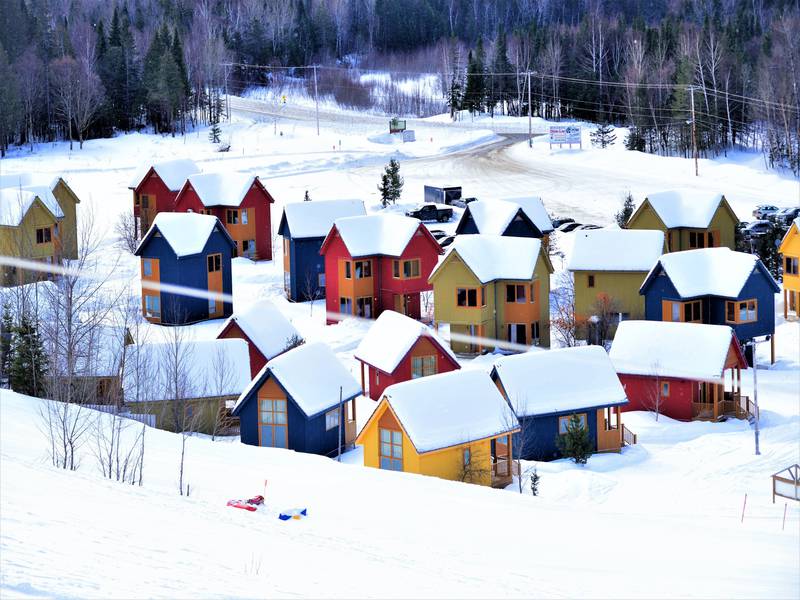 A picturesque winter scene at Pin Rouge ski resort in Quebec, Canada. Winter sports enthusiasts navigate snowy slopes, with a charming challet nestled amidst the scenery.