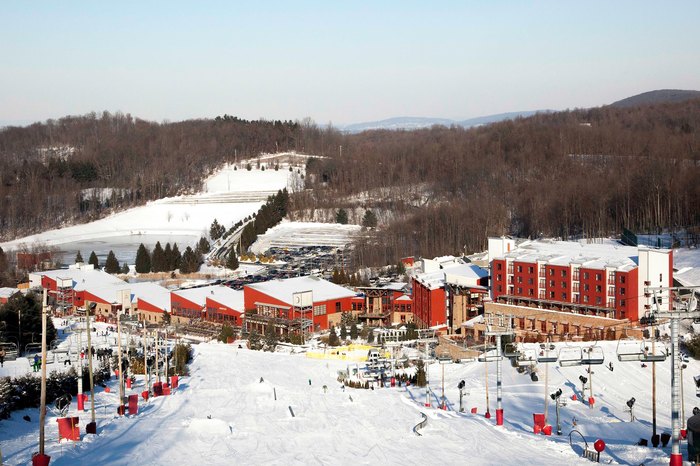 A breathtaking winter scene at Bear Creek Mountain Resort, Pennsylvania, featuring the slopes of the ski resort, a winter sports centre and a chalet set amid stunning winter scenery.