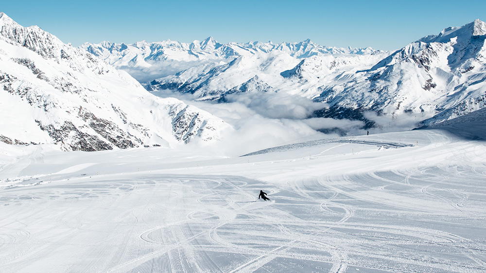 A skier enjoys the winter sports scene at the Heidbodme – Saas-Almagell ski resort in Switzerland. The image captures a charming chalet amid snow-covered slopes.