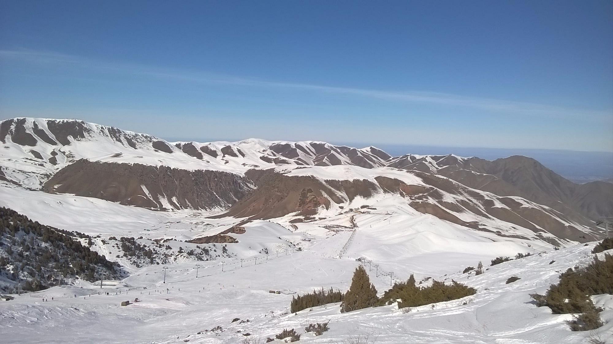 A scenic view of Chunkurchak, Kyrgyzstan featuring a charming chalet nestled amid snow-covered slopes. Nearby, a lively ski resort can be seen against the backdrop of a beautiful mountain.