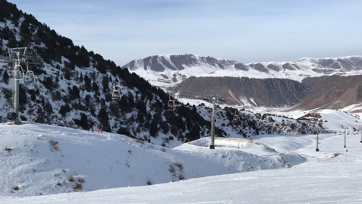 View of Chunkurchak ski resort in Kyrgyzstan featuring a challet skiers enjoying the snow-covered slopes and the majestic mountain backdrop.