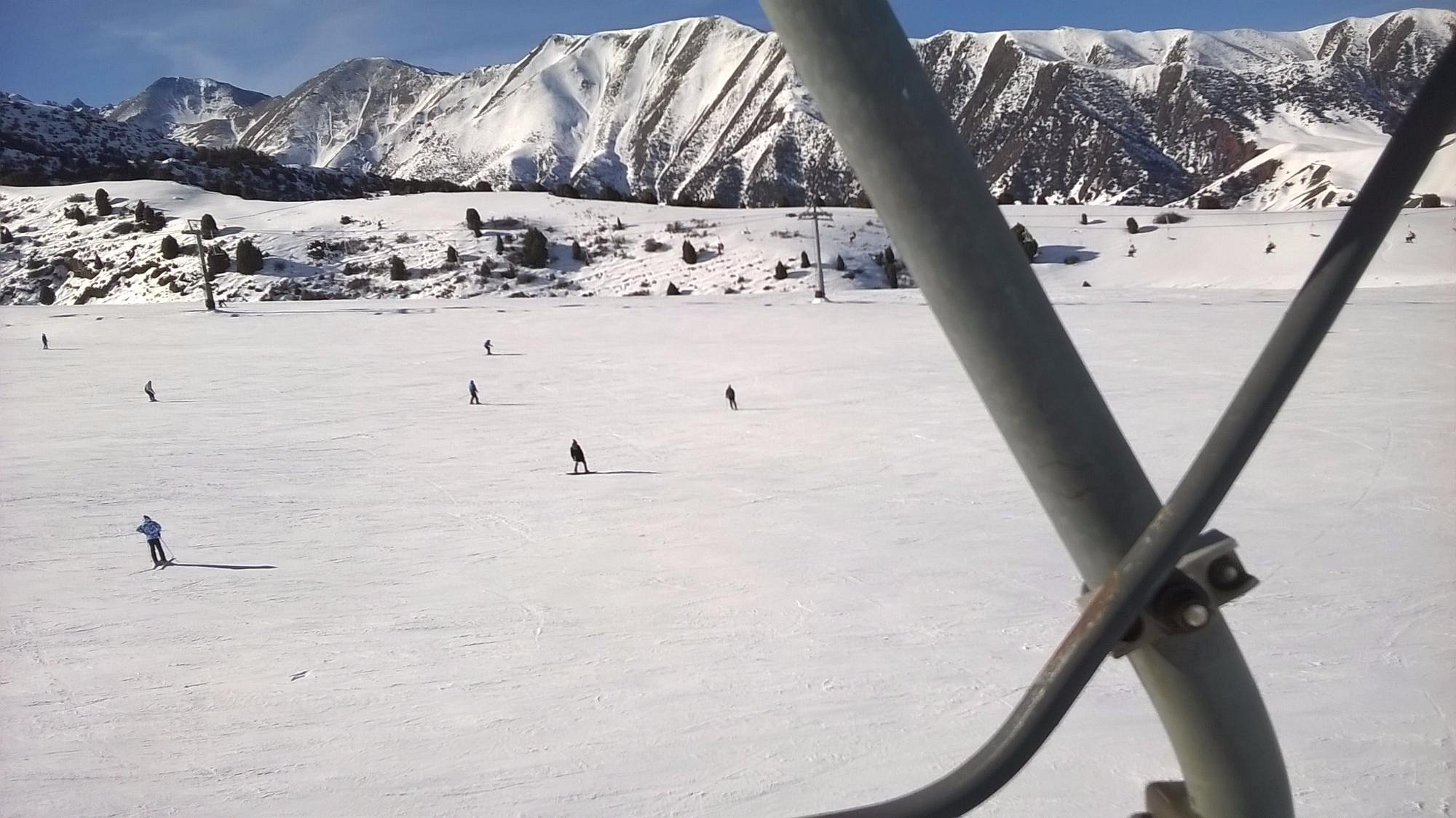 A skier gliding down the slopes at the Chunkurchak ski resort in Kyrgyzstan, with more skiers in the background. A ski lift can be seen nearby, creating the perfect winter sports scene.