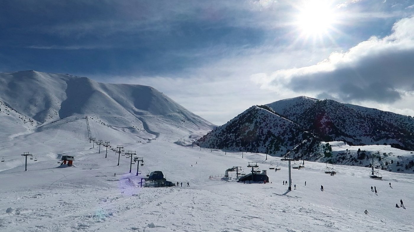 Winter scene at Chunkurchak ski resort in Kyrgyzstan, featuring snow-covered slopes dotted with a charming chalet under a serene winter sky, teeming with winter sports enthusiasts.